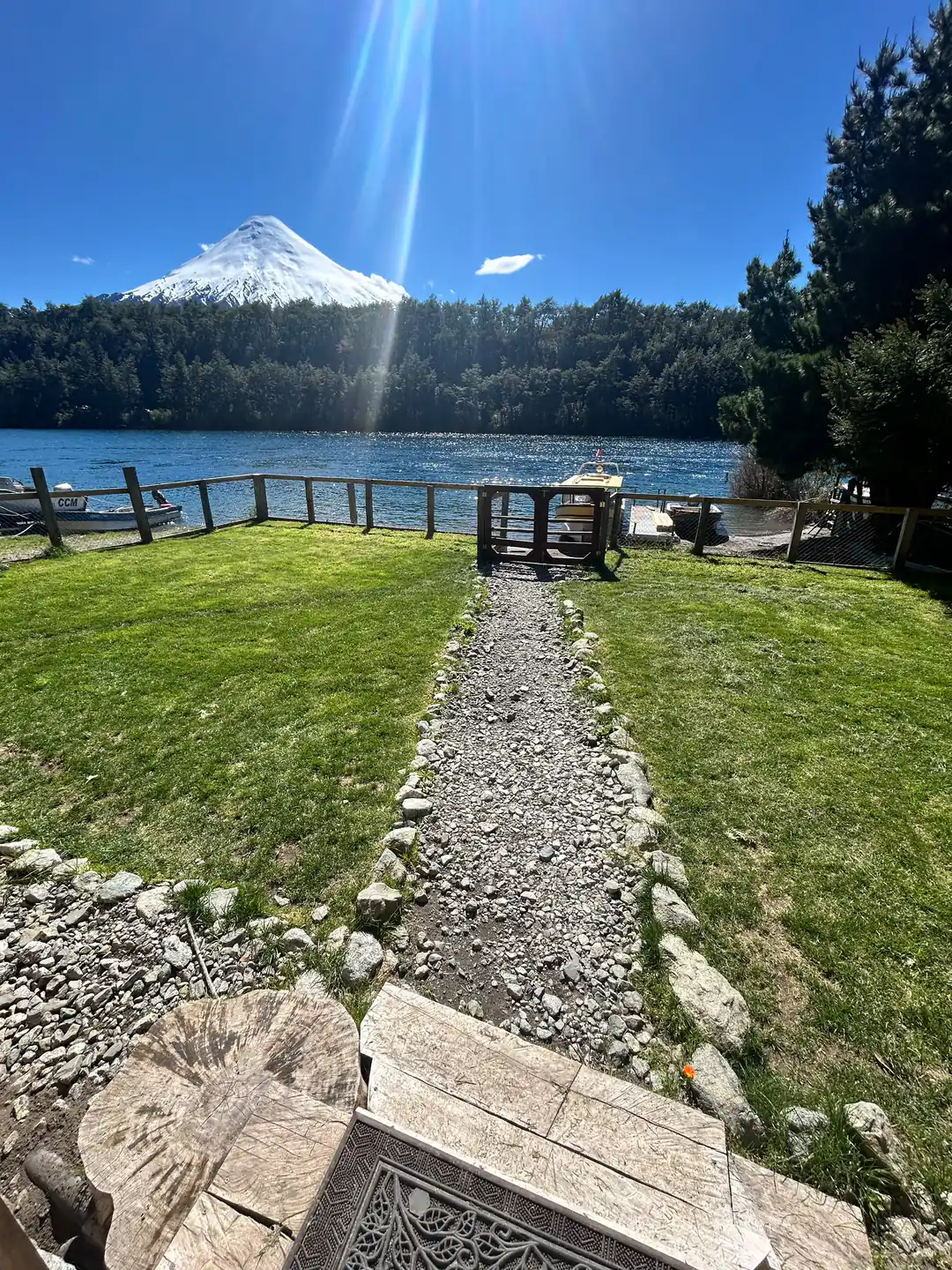 Vista desde la puerta del restaurante: el pasto, el camino de piedras hasta la reja del muelle, la lancha amarrada, el lago y el volcán Osorno.