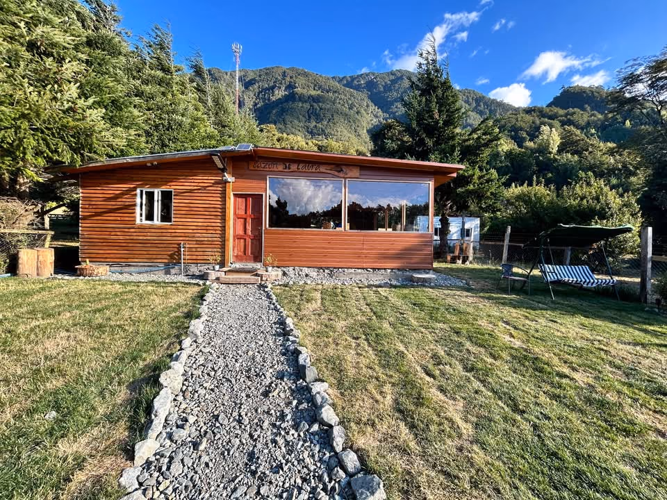 La cabaña de madera de Sazón de Laura, con el letrero en la fachada, la puerta roja y el camino de piedras.