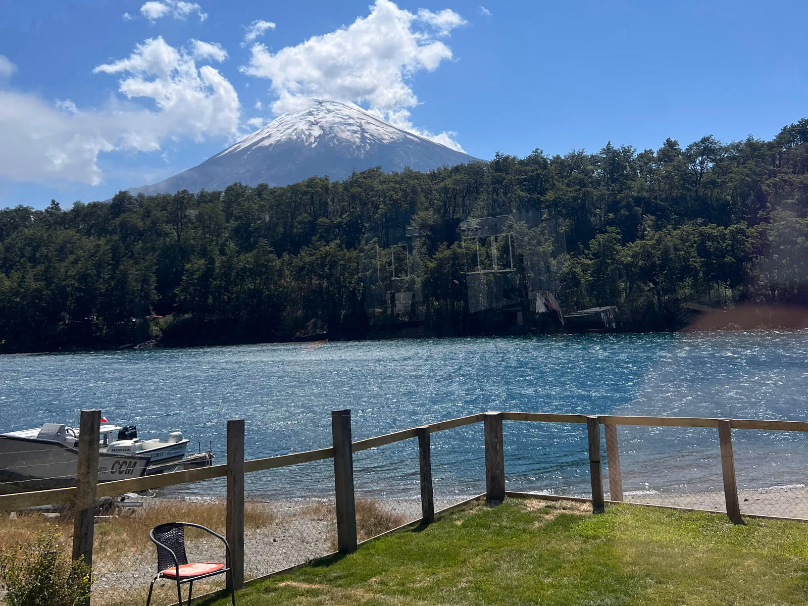El lago y el volcán Osorno desde el pasto del restaurante, detrás de una reja de madera; en la orilla, un bote amarrado.
